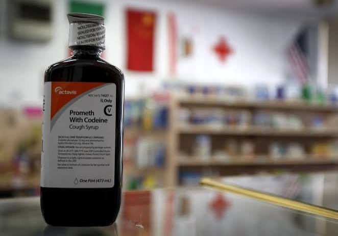 A bottle of Codeine cough syrup with a San Diego skyline in the background, representing online purchase options.